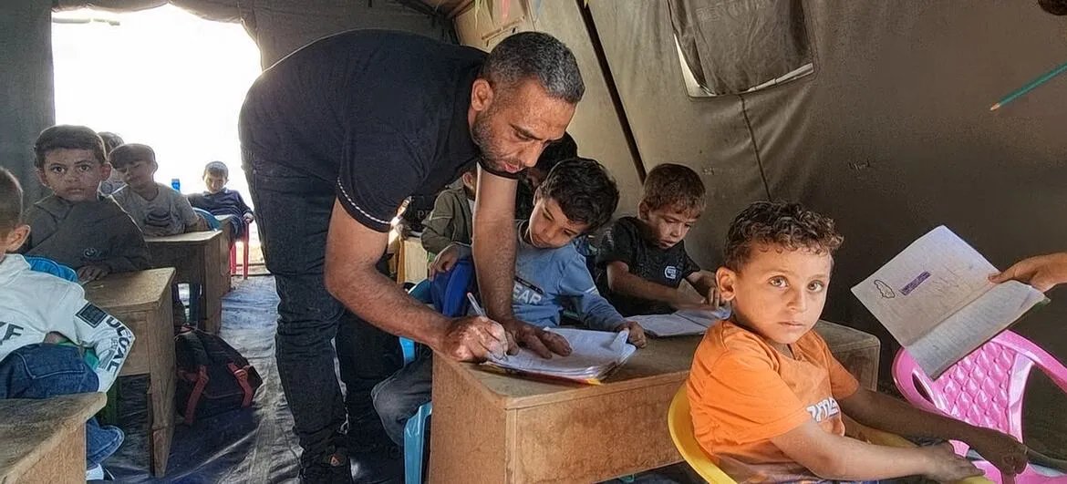 Gaza children: A teacher checks students' work in a tent classroom in Gaza City